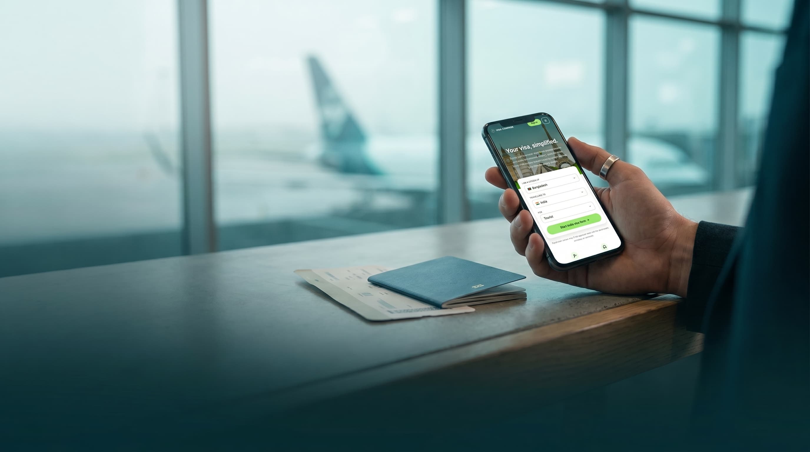 Hand holding a phone with Visa Compass application steps beside a passport at an airport gate